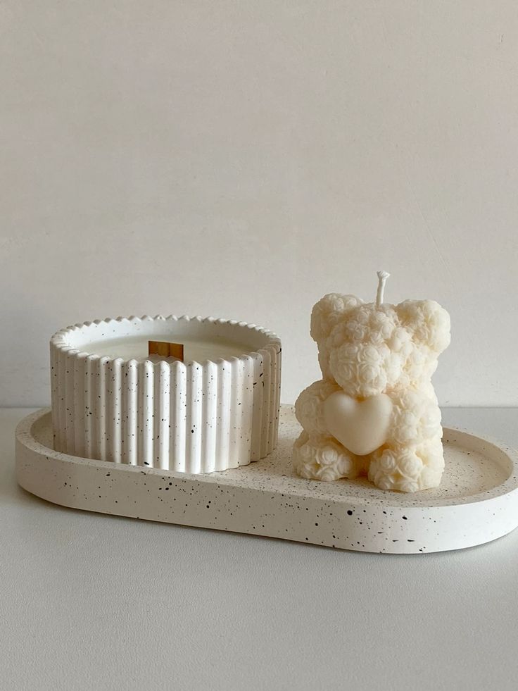 Cream bear-shaped candle beside an ivory speckled fluted candle vessel